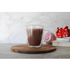 Hot chocolate protein drink mixed in a clear glass on a wooden pedestal. Two red holiday gifts are in the background.